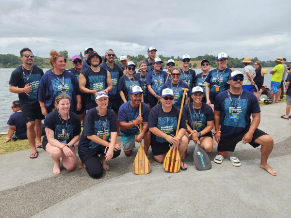 Corrections staff kneel with paddles beside Lake Karāpiro